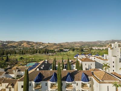 Stadt mit weißen Gebäuden, blauen Dächern, grünen Bäumen und Hügeln unter klarem blauem Himmel.
