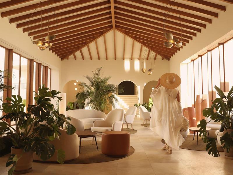 Helle Lounge mit Holzbalkendecke, großen Fenstern, Pflanzen und bequemen weißen Sesseln.