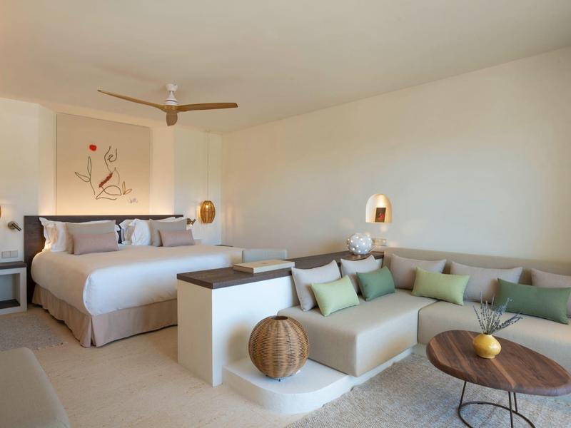 Modernes Schlafzimmer mit großem Bett, gemütlicher Sitzecke und neutralen Farben, hell und minimalistisch.