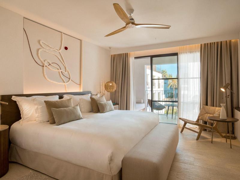 Helles Schlafzimmer mit Doppelbett, großen Fenstern, Gardinen und modernem Wandbild in neutralen Farbtönen.