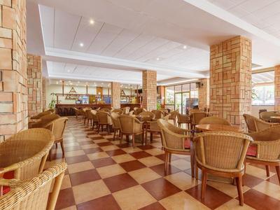 Großer, heller Speisesaal mit geflochtenen Stühlen, quadratischem Fliesenboden und Steinmauern.