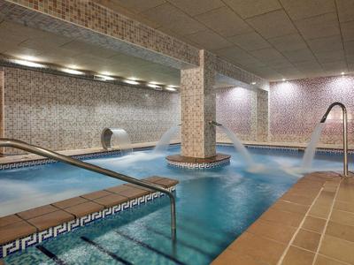 Innen-Pool mit Mosaikfliesen, Edelstahlgeländern und blauem Wasser unter Deckenleuchten.