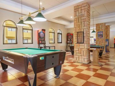 A room with two pool tables and seating, patterned floor and stone pillars.