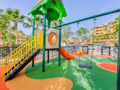 Bunter Kinderspielplatz mit Rutsche, Schaukel und weichem Bodenbelag im Freien bei Sonnenschein.