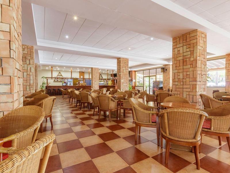 Großer, heller Speisesaal mit geflochtenen Stühlen, quadratischem Fliesenboden und Steinmauern.