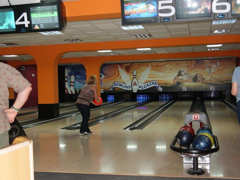 Menschen beim Bowling in einer Halle mit neun Bahnen, orangene Wände, Bowlingkugeln auf Halter.