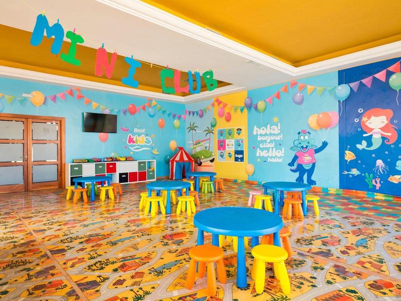 Bunter Kinderspielraum mit kleinen Tischen, Hockern, Spielzeug und maritimem Wandbild.