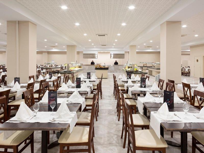 Großer, heller Speisesaal mit mehreren Reihen Tischen, weißen Tischdecken und gefalteten Servietten.