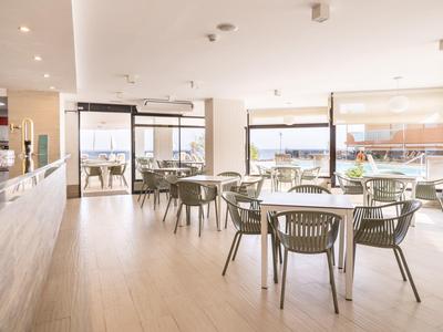 Helles, modernes Restaurant mit Holzfußboden, Glasfenstern und grauen Stühlen an runden Tischen.