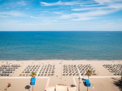 Strand mit organisiert aufgestellten Sonnenschirmen und Liegestühlen unter blauem Himmel am Meer.