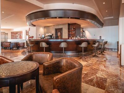 Moderner Barbereich mit braunen Ledersesseln, runder Theke und Marmorfußboden.