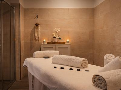 Beige Wellnessraum mit Massagebank, weißen Handtüchern, Kerzen und entspannender Atmosphäre.