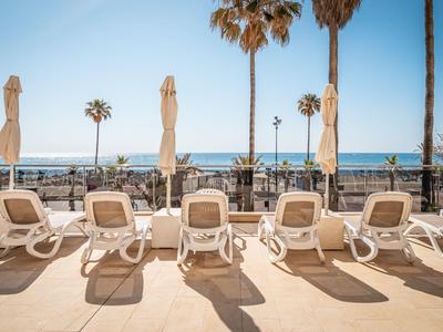 Leere Liegestühle und geschlossene Sonnenschirme an einer Terrasse am Meer bei Sonnenschein.
