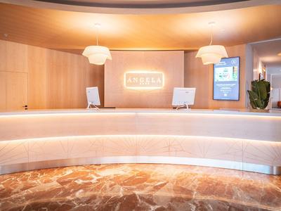 Moderne Empfangstheke mit Beleuchtung, Holzverkleidung, zwei Monitoren und Marmorboden in warmen Tönen.