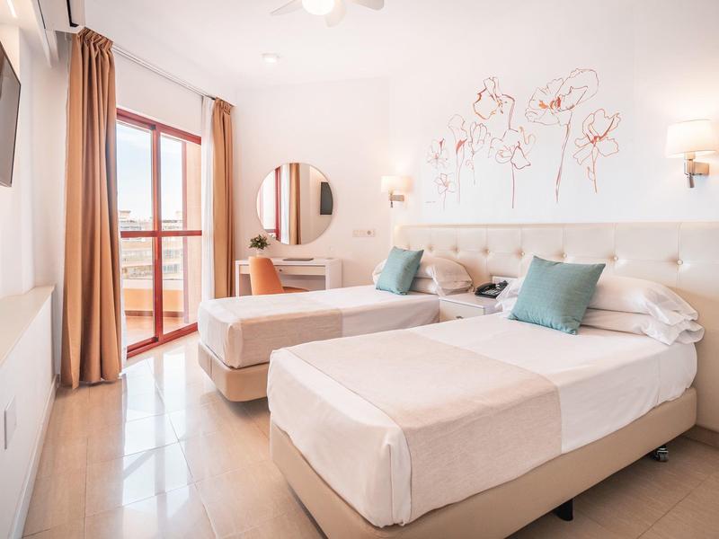 Hell eingerichtetes Schlafzimmer mit zwei Einzelbetten, blauen Kissen und Balkonzugang.