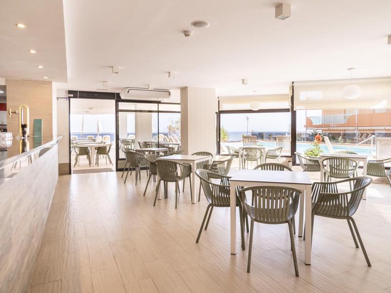 Helles, modernes Restaurant mit Holzfußboden, Glasfenstern und grauen Stühlen an runden Tischen.