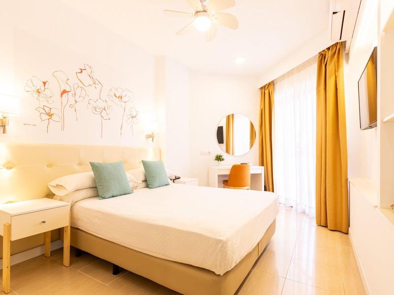 Helles, modernes Schlafzimmer mit großem Bett, goldenen Vorhängen und schlichtem Holzmobiliar.