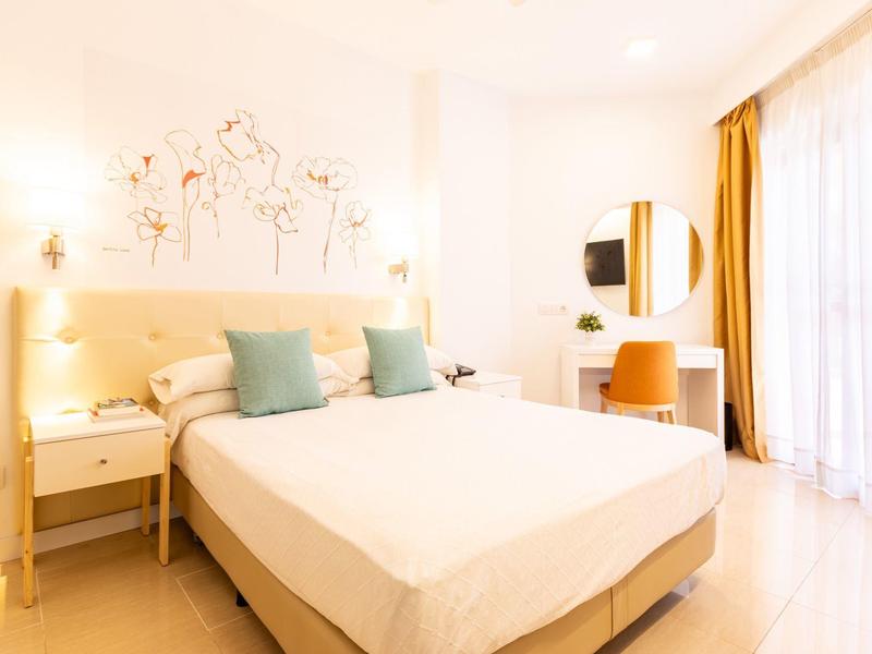 Helles, modernes Schlafzimmer mit großem Bett, zwei blauen Kissen, Nachttischen und rundem Spiegel.