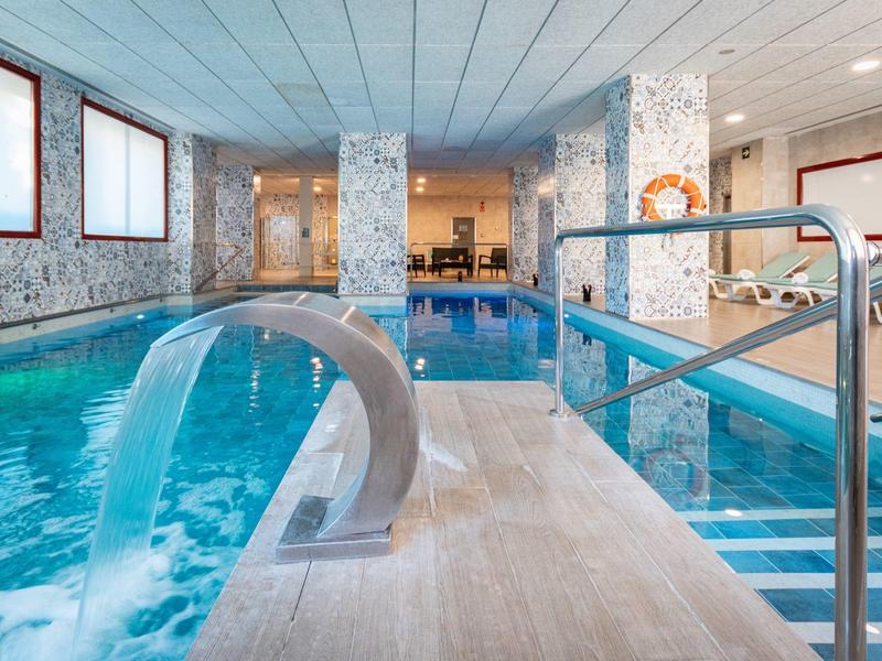 Innenraum mit gedecktem Schwimmbad, Wassersprudler, Treppen und modernen Mosaikfliesen.