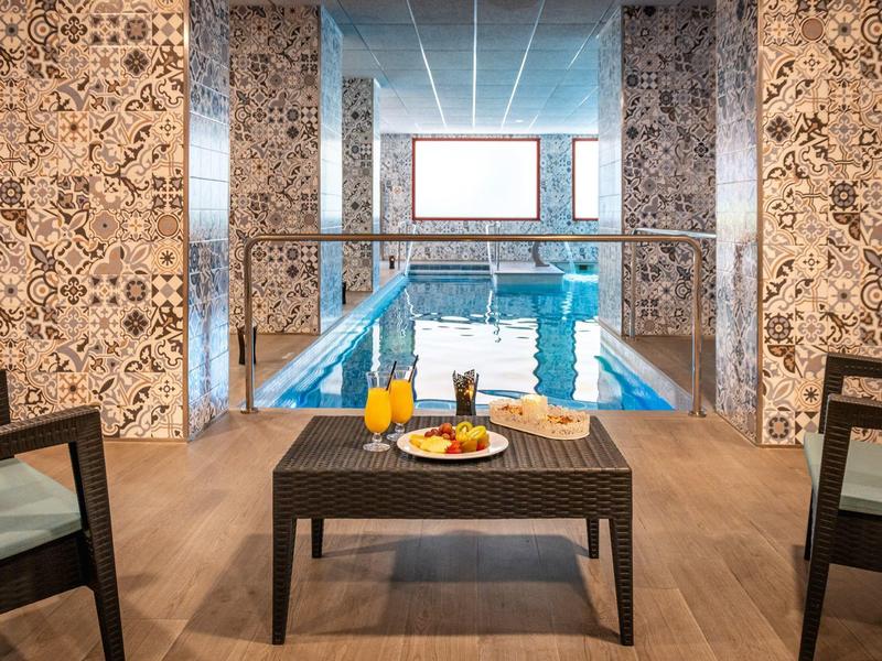 Moderner Innenpool mit Musterwänden, zwei Sesseln und Tisch mit Getränken und Snacks.