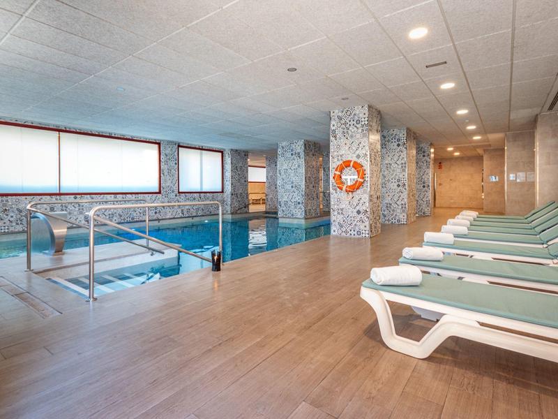 Innenraum eines Schwimmbads mit Pool, Liegestühlen und Fliesenwänden in hellem Design.