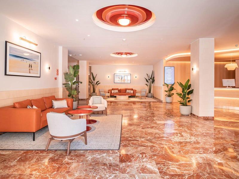 Großer Hotelflur mit glänzendem Marmorfußboden, orangen Sofas, weißen Sesseln und Pflanzen.