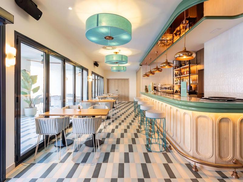 Moderner Gastraum mit geometrischem Bodenmuster, türkisfarbenen Lampen und geschwungenem Bartresen.