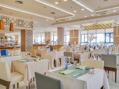 Großer Restaurantraum mit weißen Tischen, hellen Stühlen und modernen Dekorelementen.