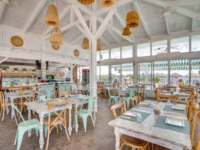 Heller, luftiger Gastraum mit weißen Holzbalken, Pastelltischen und Stühlen, großen Fenstern.