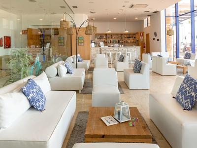 Helles Wohnzimmer mit weißen Sofas, blauen Kissen, Holztisch und großem Fenster mit Sonnenlicht.