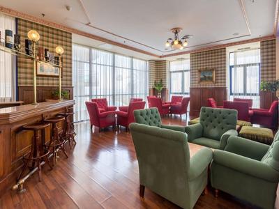 Wohnzimmer mit grünen Sesseln, roten Stühlen, Holzboden und großem Fenster für viel Tageslicht.