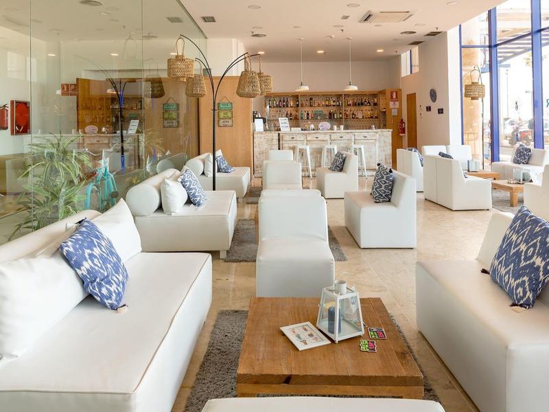 Helles Wohnzimmer mit weißen Sofas, blauen Kissen, Holztisch und großem Fenster mit Sonnenlicht.