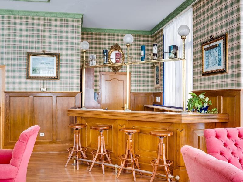 Gemütliche Hausbar mit Holztheke, Barhockern, karierten Wänden und rosafarbenen Sesseln.