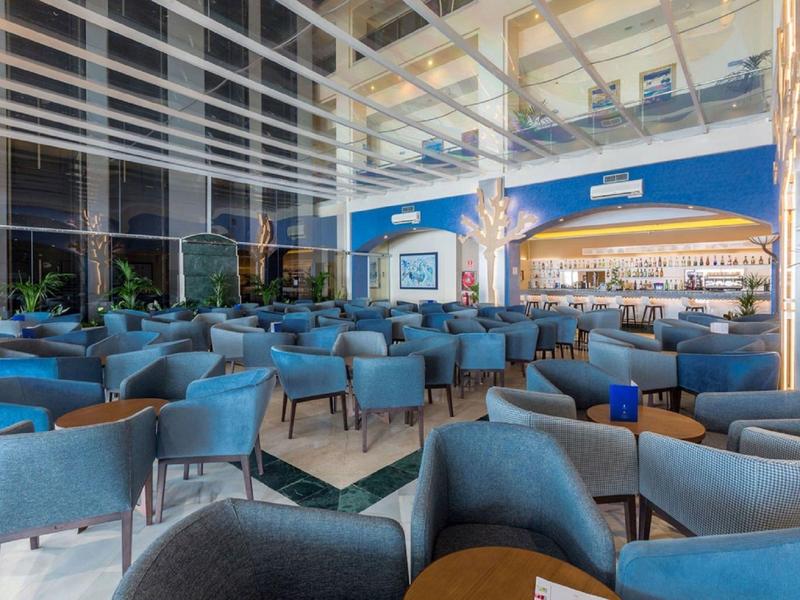 Moderner, heller Innenraum mit vielen blauen Sesseln und großen Fenstern bis zur Decke.