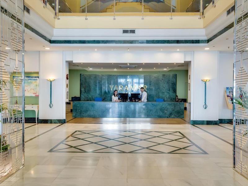 Großer, heller Empfangsbereich mit marmornem Tresen, Glaswänden und geometrischem Bodenmuster.