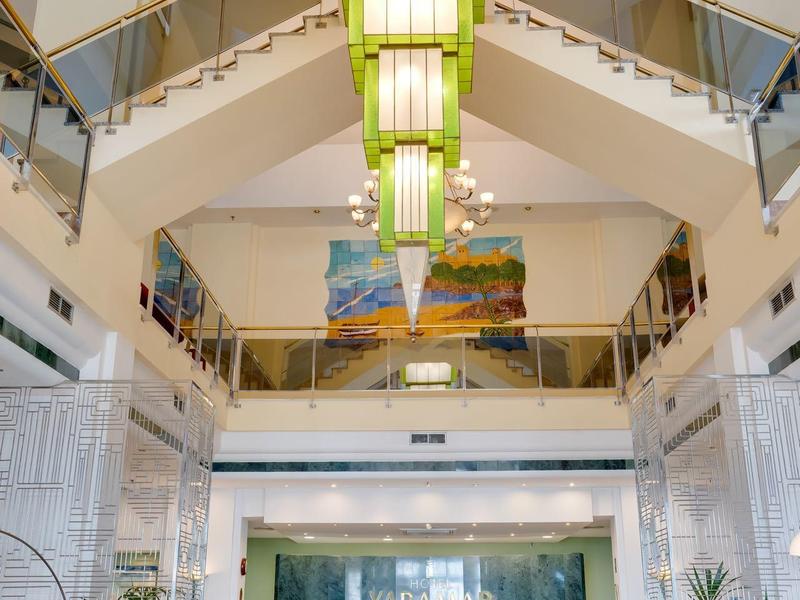 Helles, modernes Treppenhaus mit grünen Lampen und türkisfarbenen Sitzbänken in Eingangsbereich.