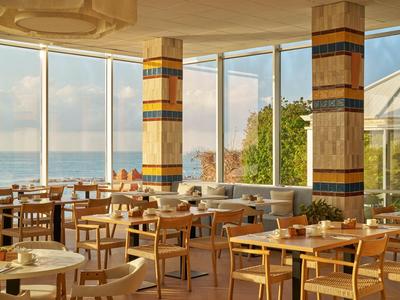 Restaurant d'hôtel lumineux avec tables en bois et vue sur la mer à travers de grandes fenêtres.
