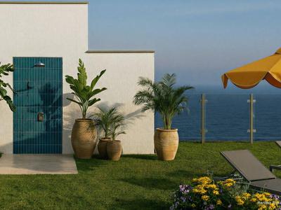 Terrazza con lettini, ombrellone e piante accanto a un edificio bianco con vista sul mare.