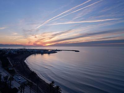 Plage et côte au coucher du soleil avec des nuages allongés dans le ciel.