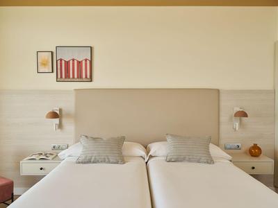 Chambre d'hôtel moderne avec deux lits simples, coussins gris et décoration murale minimaliste.