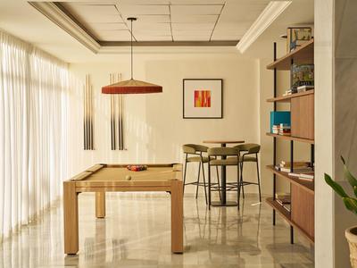 Salle lumineuse avec table de billard, tabourets de bar et bibliothèque ouverte dans un hôtel.