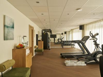 Une salle de sport moderne avec des tapis de course, des appareils d'exercice et de la lumière naturelle.