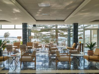 Salon d'hôtel moderne avec fauteuils en cuir, murs en verre et vue sur la terrasse et les arbres.