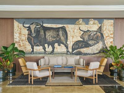 Salon confortable avec canapé, fauteuils et grande fresque murale de bœufs dans un cadre hôtelier.
