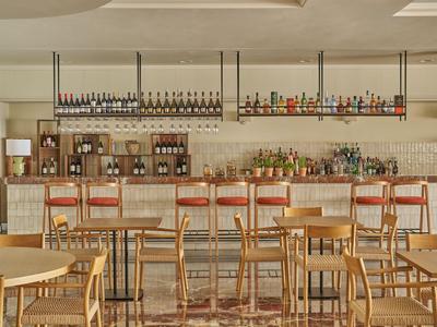 Espace bar d'hôtel moderne avec des chaises en bois et un comptoir bien approvisionné sous une lumière chaude.