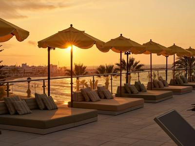 Coucher de soleil sur une terrasse de piscine d'hôtel avec des transats et parasols au bord de la mer.