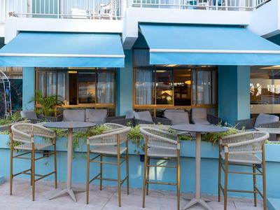 Area esterna di un bar dell'hotel con sedie in legno e tende blu in una giornata di sole.