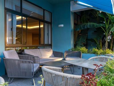 Accogliente area salotto all'aperto con poltrone e divani davanti a una camera d'hotel con grande finestra.