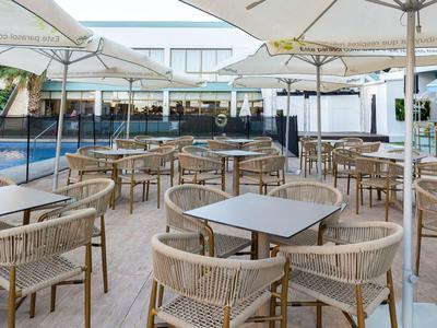 Area esterna di un hotel con più tavoli, sedie e grandi ombrelloni accanto a una piscina.