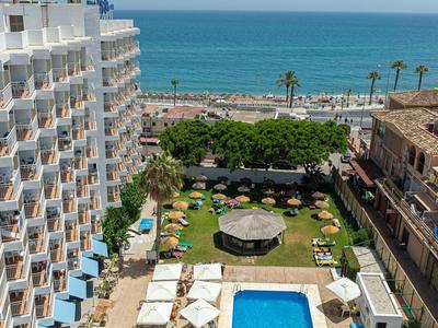 Hotel con piscina e giardino vicino al mare, circondato da edifici e palme.